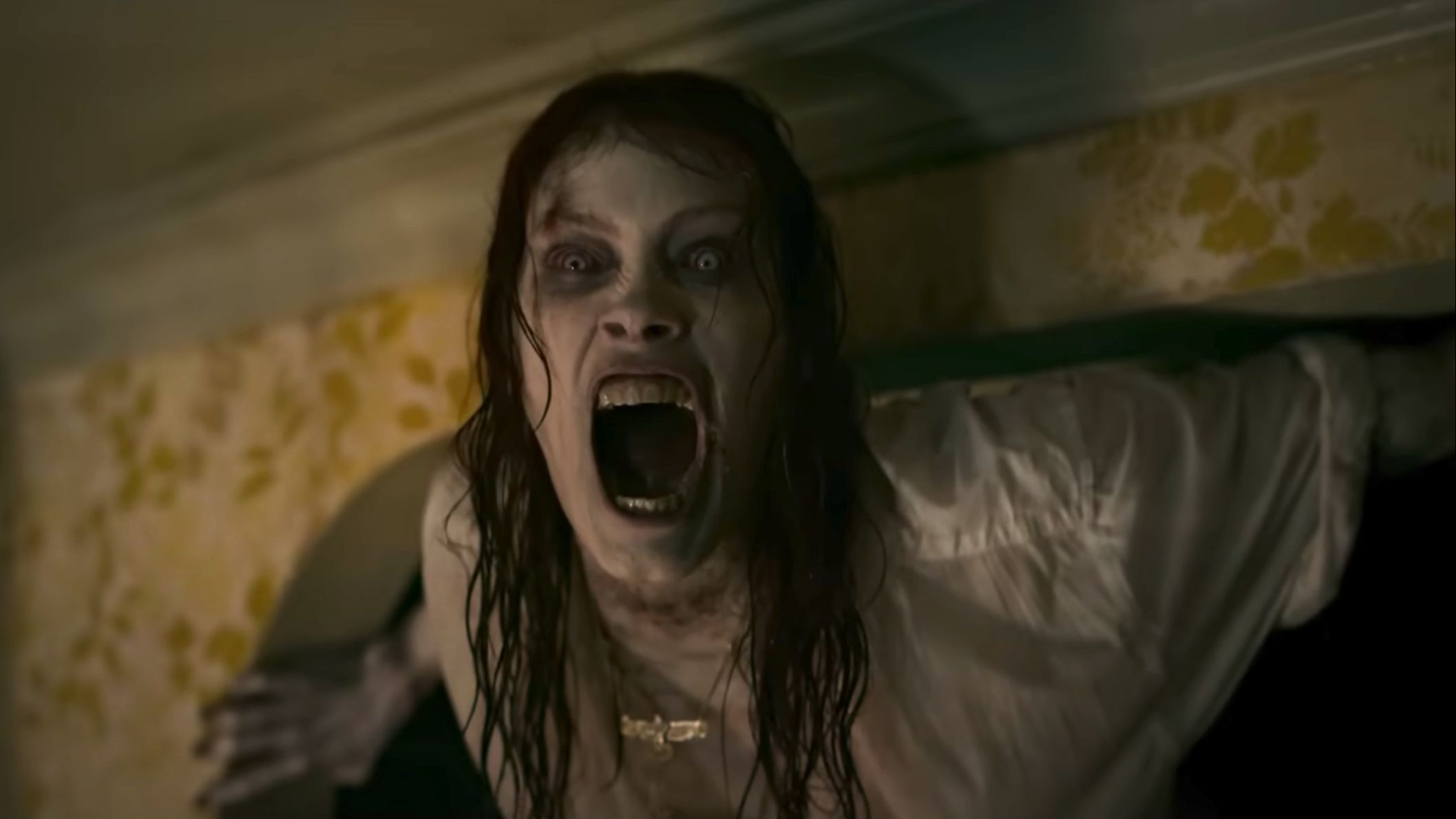 A possessed Ellie shrieks as she perches in a corner between a wall and ceiling in Evil Dead Rise
