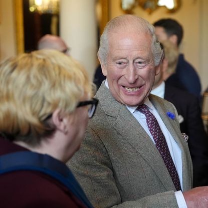 King Charles wearing a gray suit and laughing, talking to a woman