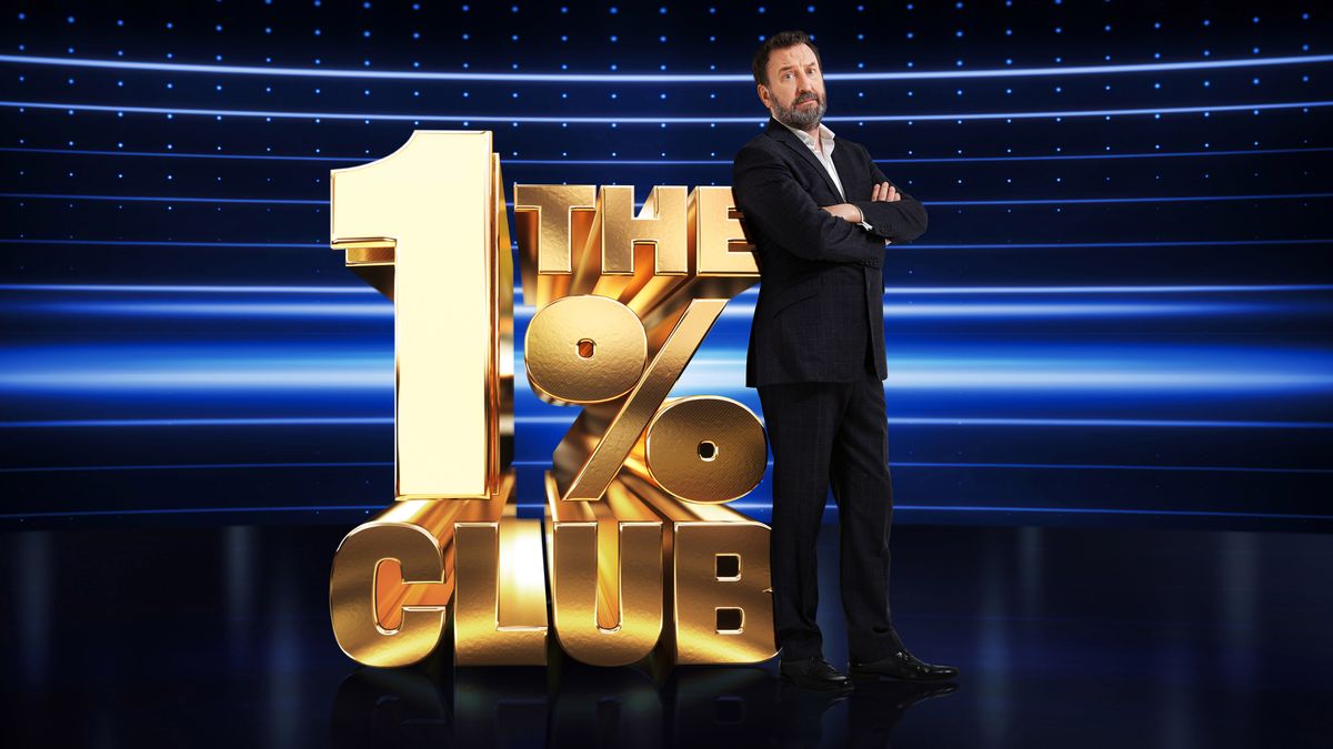 Lee Mack stood next to the 1% club season 2 logo