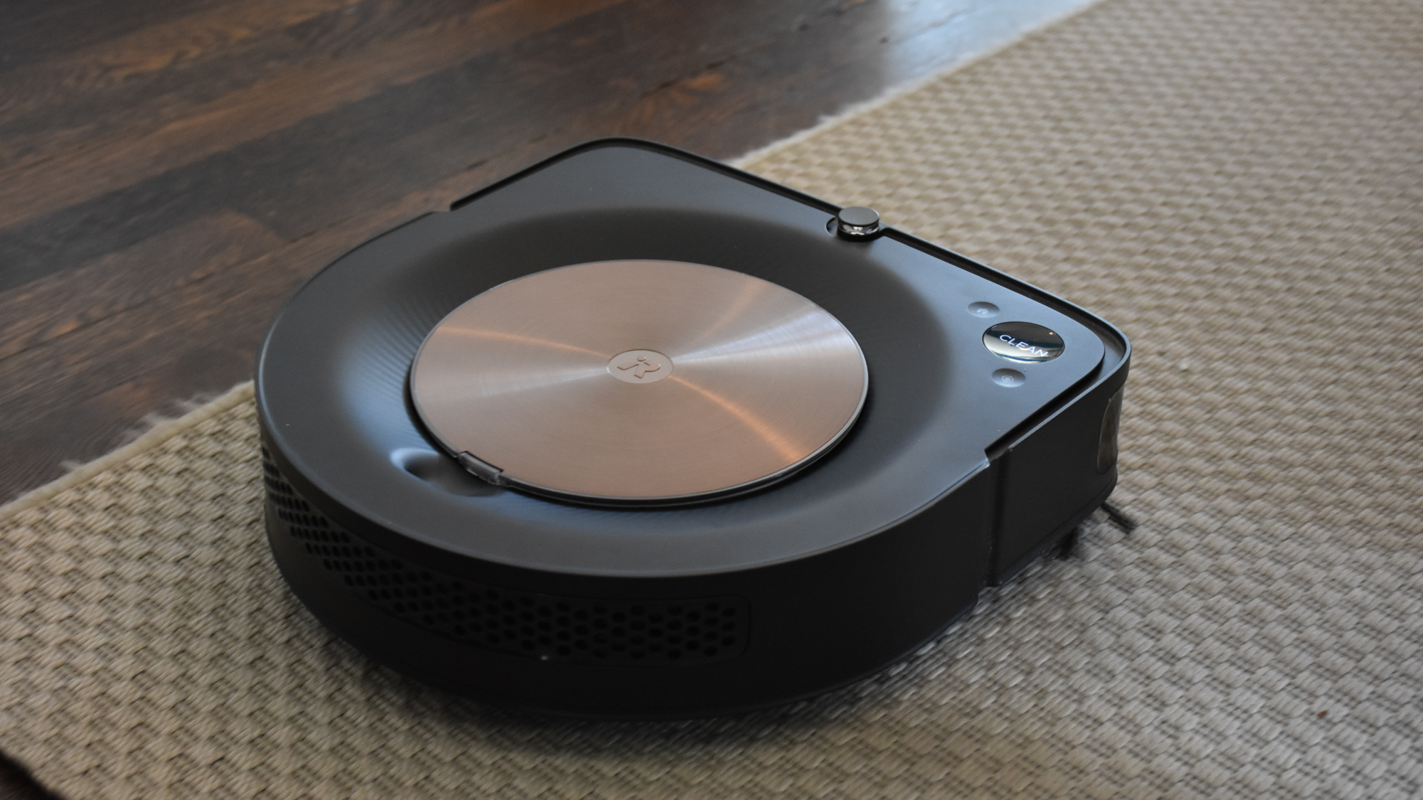 An iRobot Roomba s9+ cleaning a brown rug on top of hardwood floor