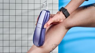 Hand holding ULike Air 10 IPL machine on a leg, photographed in front of a blue background. 