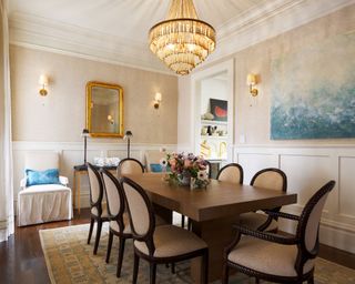 Classic dining room with large chandelier, large wooden table, artwork and wall lights on walls