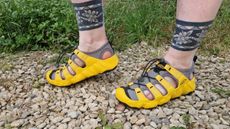 Fitness writer Lou Mudge models a pair of Keen Hyperport 2 sandals on a gravel path. Behind her we see a shrub and grass.