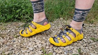 Fitness writer Lou Mudge models a pair of Keen Hyperport 2 sandals on a gravel path. Behind her we see a shrub and grass.