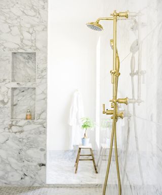 Marble shower enclosure with brass fittings, small wooden stool in background with bonsai tree