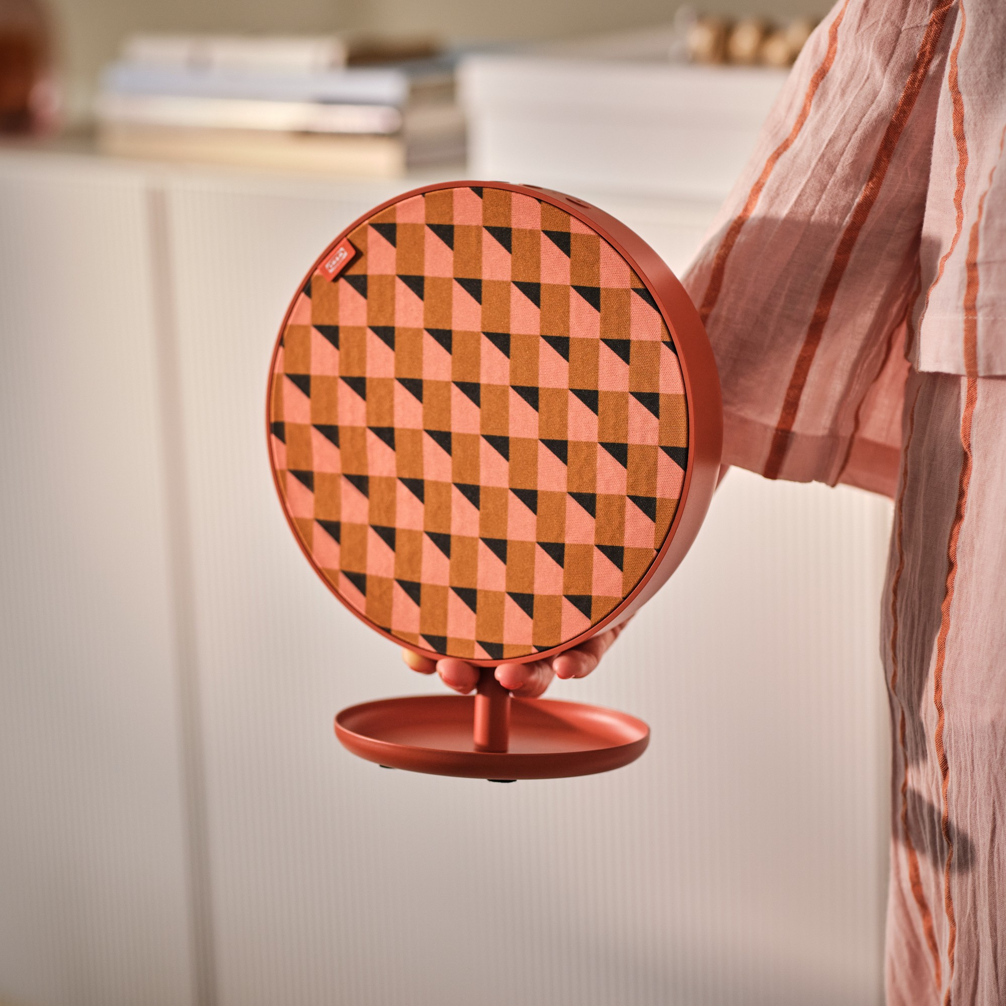 A woman holding the small, orange, patterned IKEA SOLSKYDD Bluetooth speaker from the retailer&#039;s collaboration with Teklan