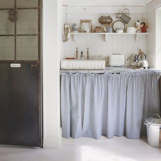 Utility room with sink and shelves, and under-the-sink storage thats been hidden with cafe curtains