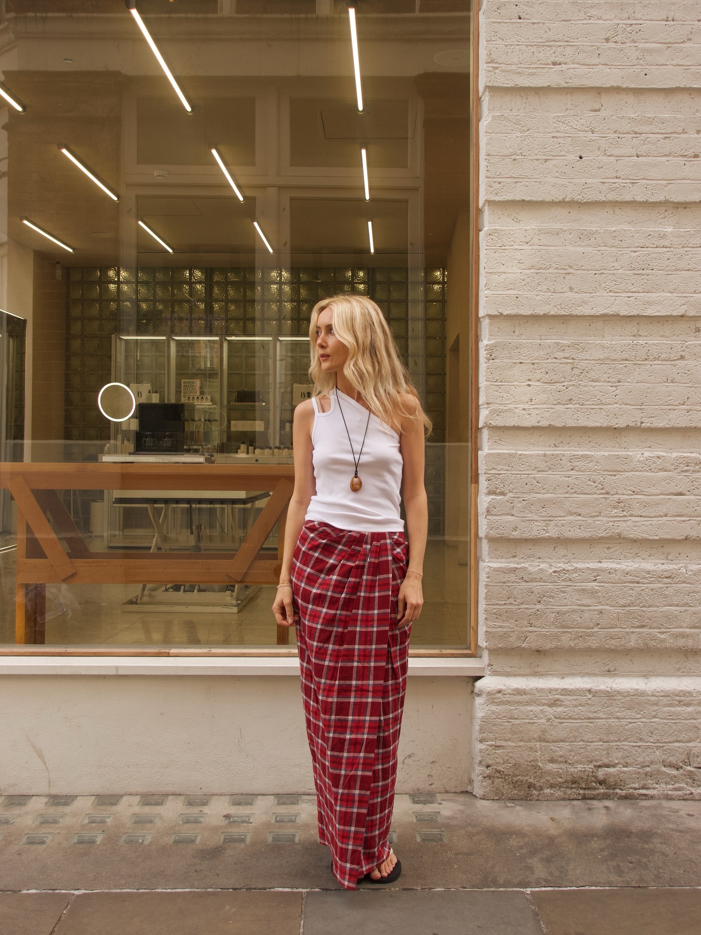An image of @chloekathbutler wearing a check skirt with a white tank top and long pendant necklace, one of the key autumn London fashion trends 2025.
