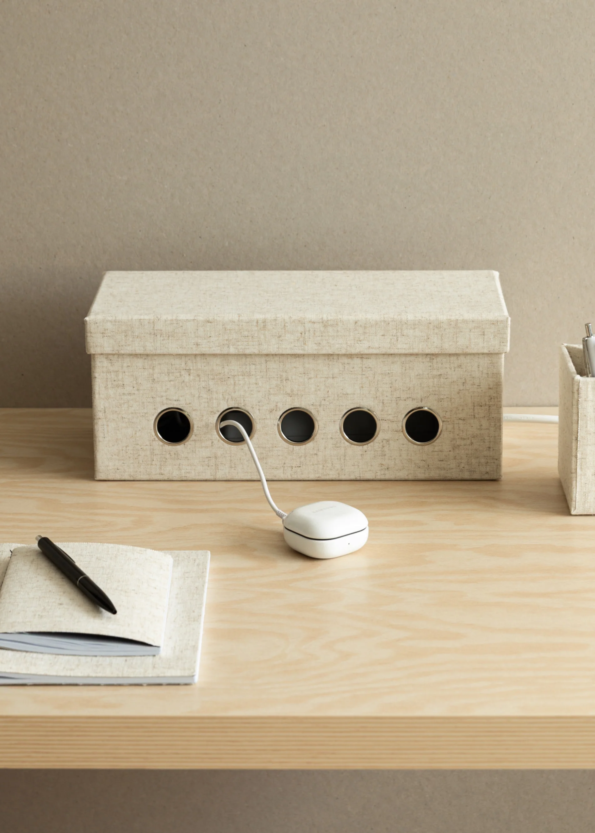 A textured cream cable holder box on a desk beside a stationery box and a pair of books