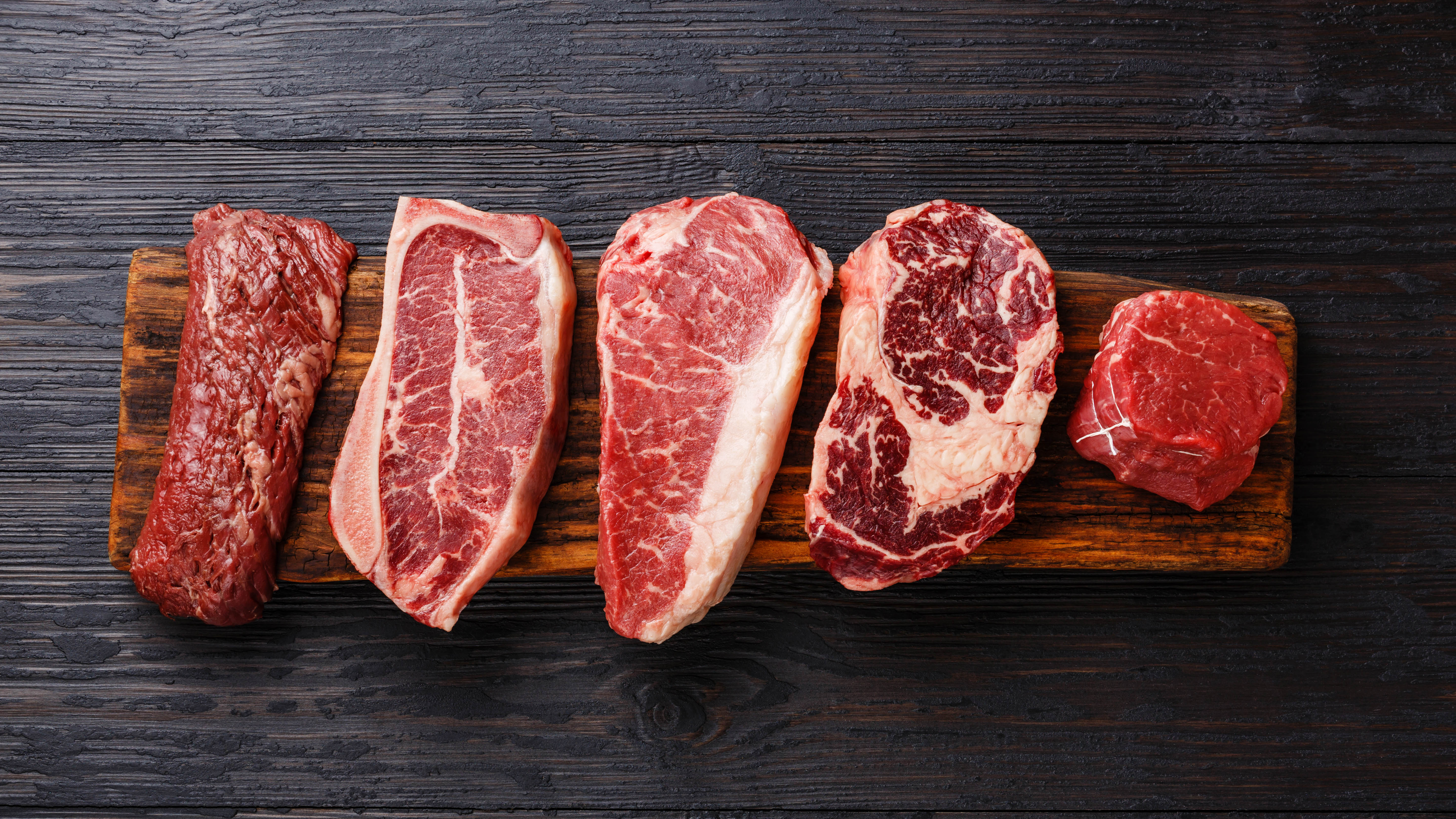 Raw steaks lined up on a wooden board