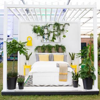 flower show with white bed, grey cushions with surrounded potted plants