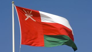 The flag of Oman flying against a clear blue sky