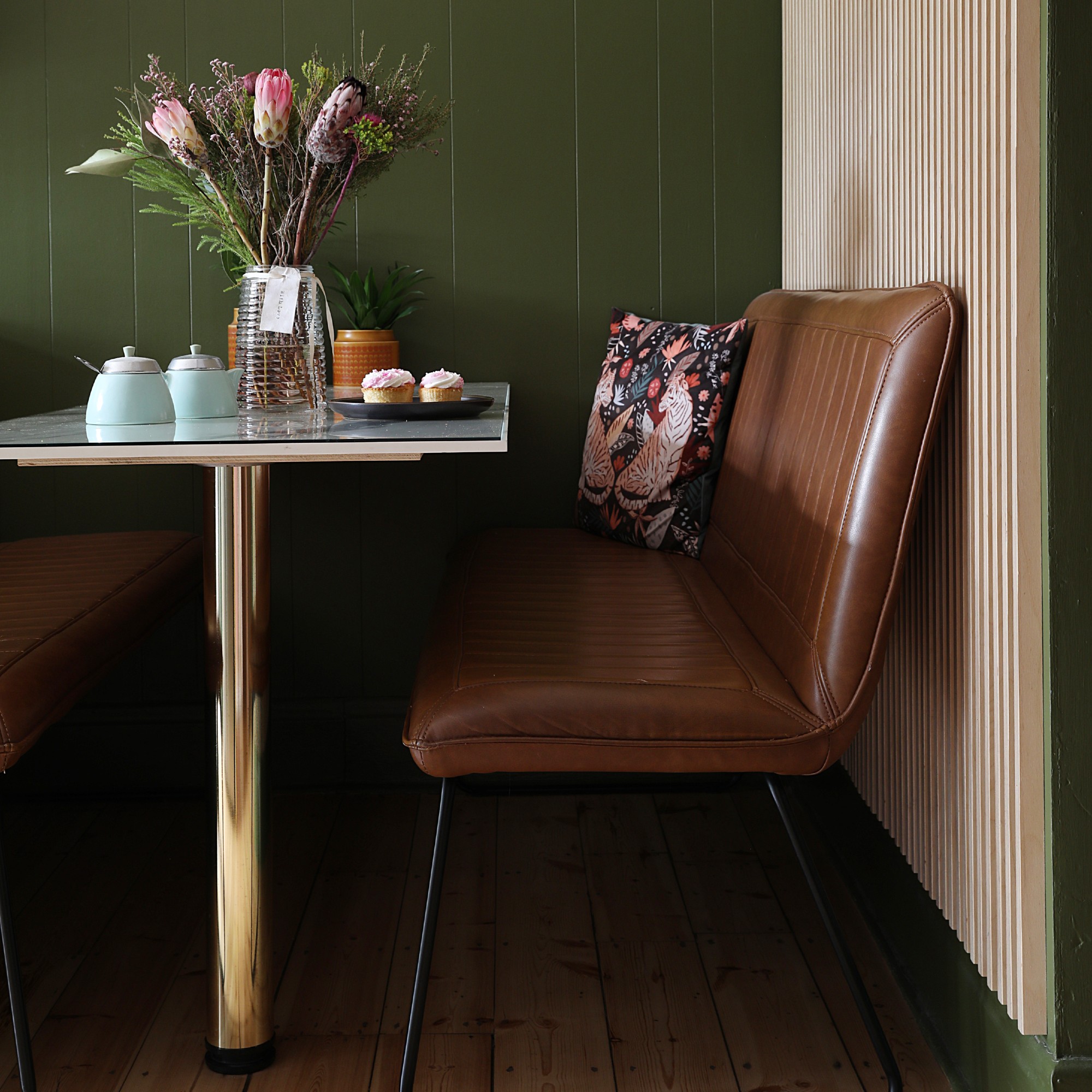 A dining nook with brown leather benches and a fixed chrome and glass dining table
