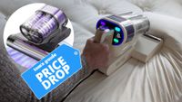 The image shows a close-up view of a hand running a mattress vacuum along the surface of a pillow. Overlaid on top of the image a blue price tag reads 'Tom's Guide price drop'