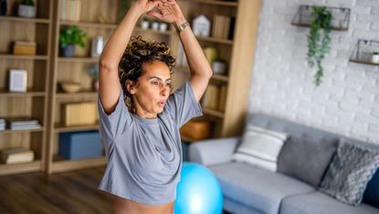Woman exercising at home, with her arms raised above her head