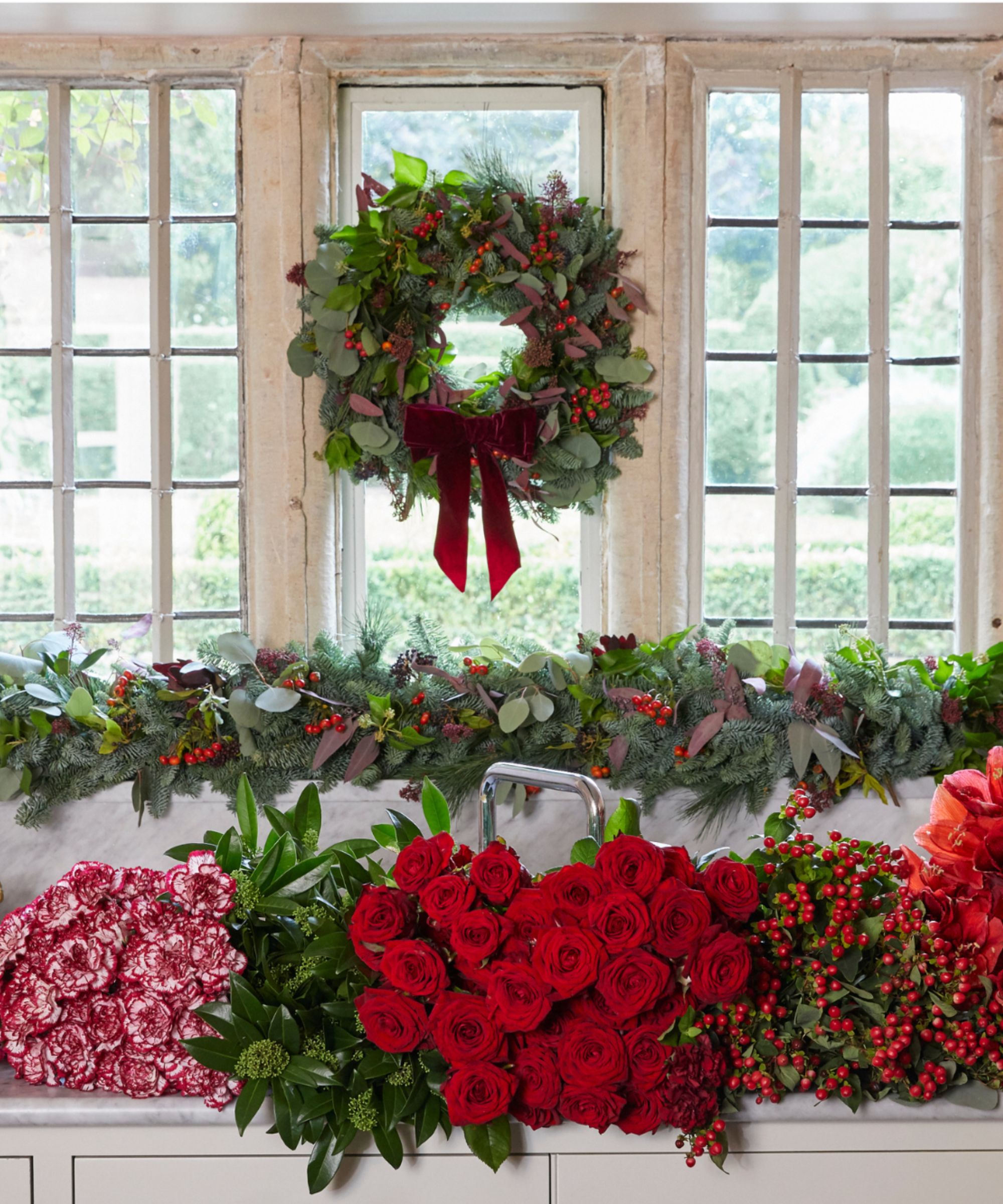 Christmas wreath and garland in kitchen window with sink full of flowers