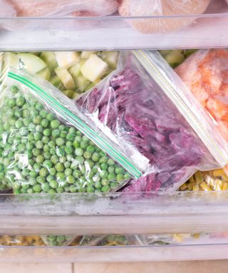 An image of a freezer drawer with see-through bags of colourful vegetables including peas, zucchini, sweetcorn, carrots and cabbage,