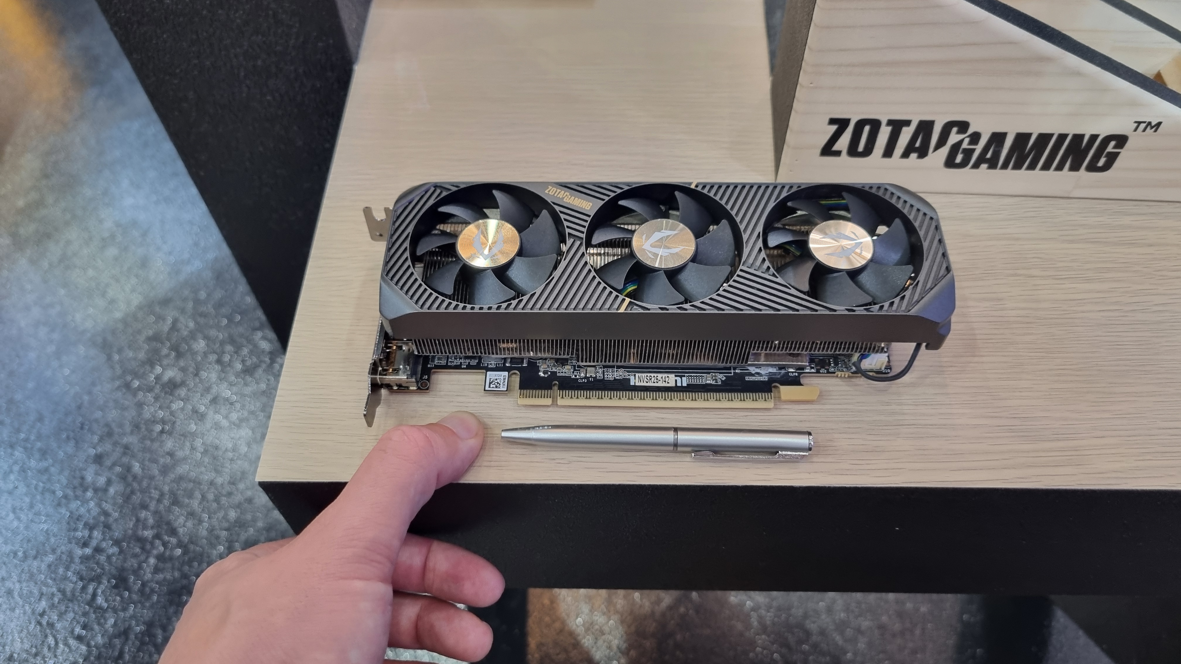 The Zotac Gaming RTX 5060 Low Profile on a desk, with a pen and a thumb for scale