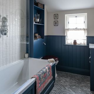 Bathroom with blue half-panelled walls, tiled floor and bath with blue panel