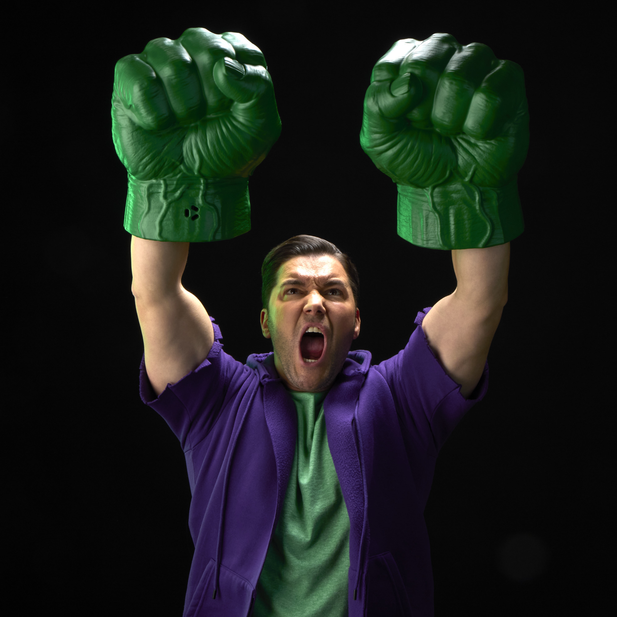 A roaring man with two Hulk Fists pretends to punch with them against a black background