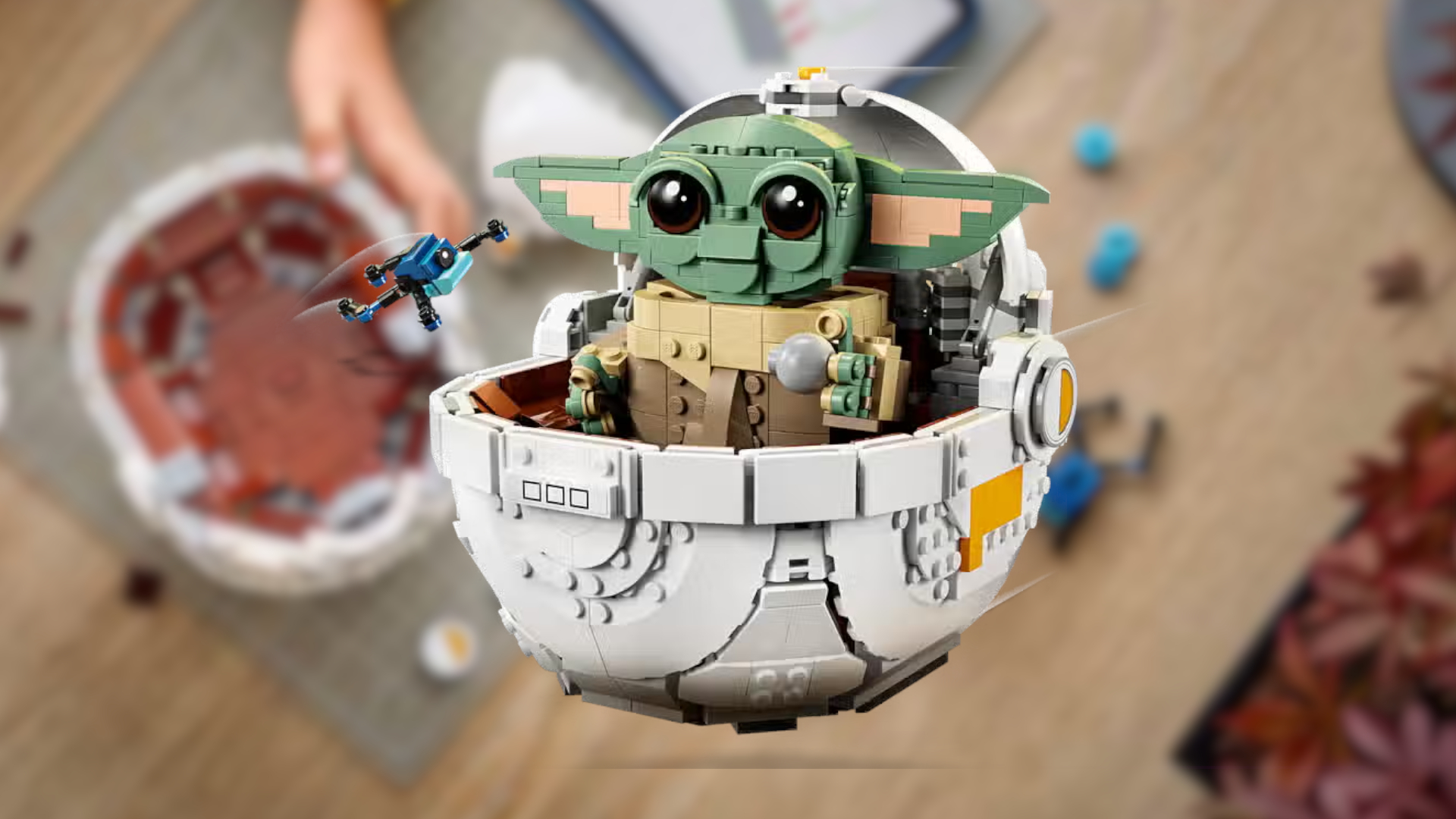 Lego Grogu flying in hover pram against a blurry background of a work surface