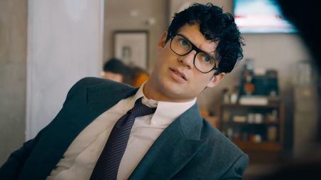 David Corenswet leans to his side in an office chair as he talks in Superman. 