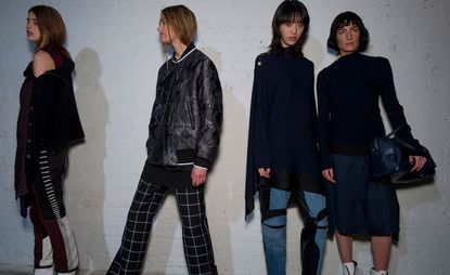Four female models, one in a black jacket and black, red and white trousers, one in a black shiny jacket and black and white check trousers, one in a navy sweater and blue denim jeans with black details, and one wearing a navy sweater and skirt