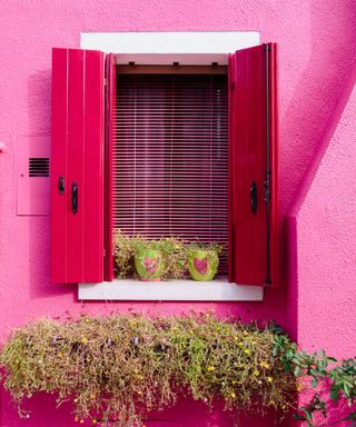 A pink house with pink window shutters that are open.