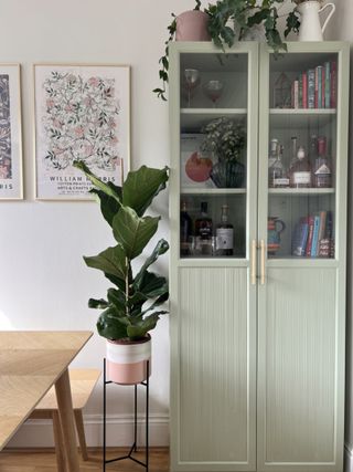 An upcycled IKEA billy bookcase painted in a light sage green with brass handles