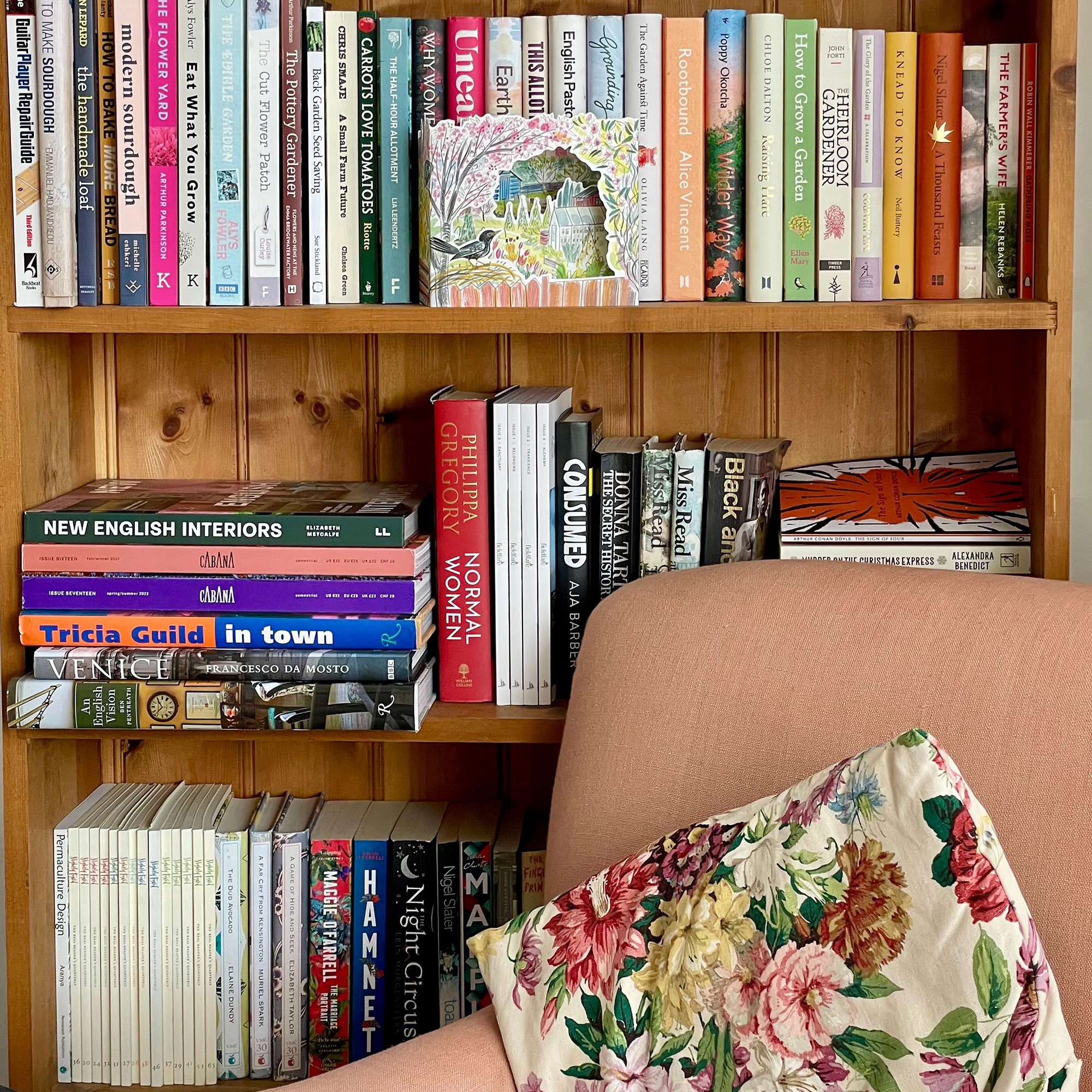 Full wooden bookshelves behind pale pink armchair with floral cushion