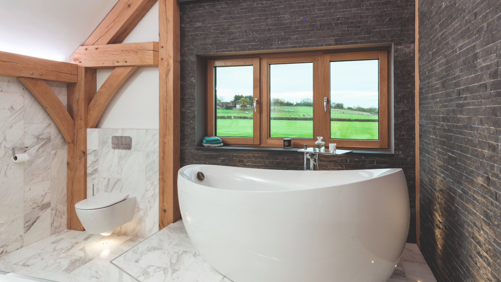 Freestanding bath on marble flooring next to bathroom window facing field