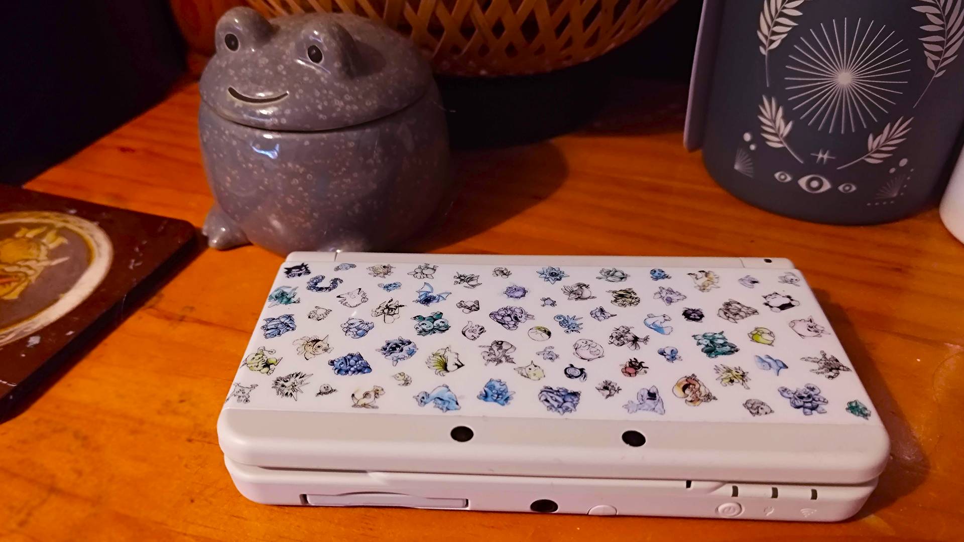 New 3DS with Pokemon sprite cover on bedside table.