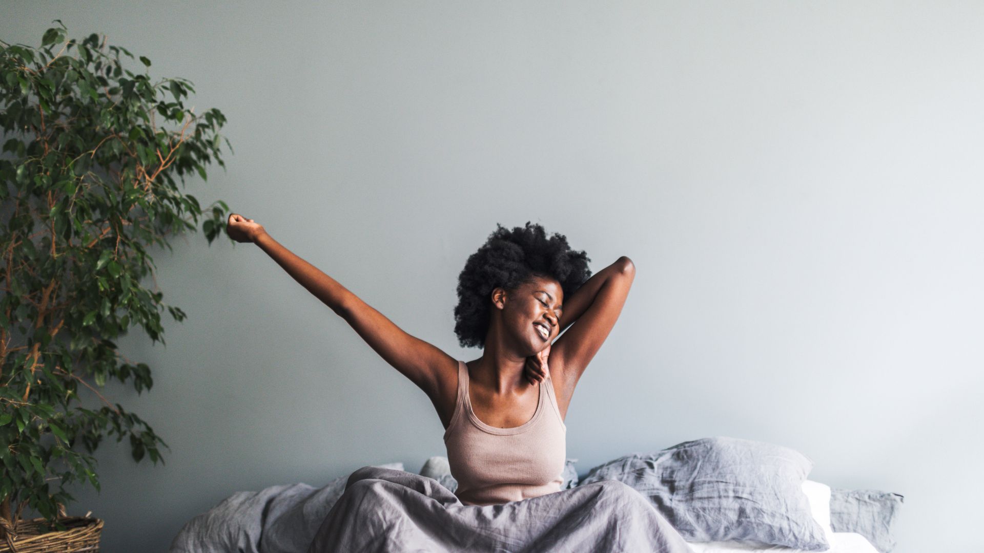 Woman smiles and stretches as she sits up in bed.