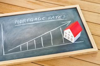 A chalkboard with a model house on it and chalk writing saying "mortgage rates" with an arrow pointing upward 