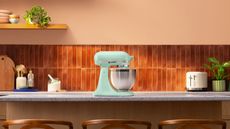 A spearmint blue stand mixer on a kitchen island, with terracotta colored tiles in the background. 