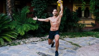 Muscular male holding a kettlebell overhead while performing a lunge during outdoor workout