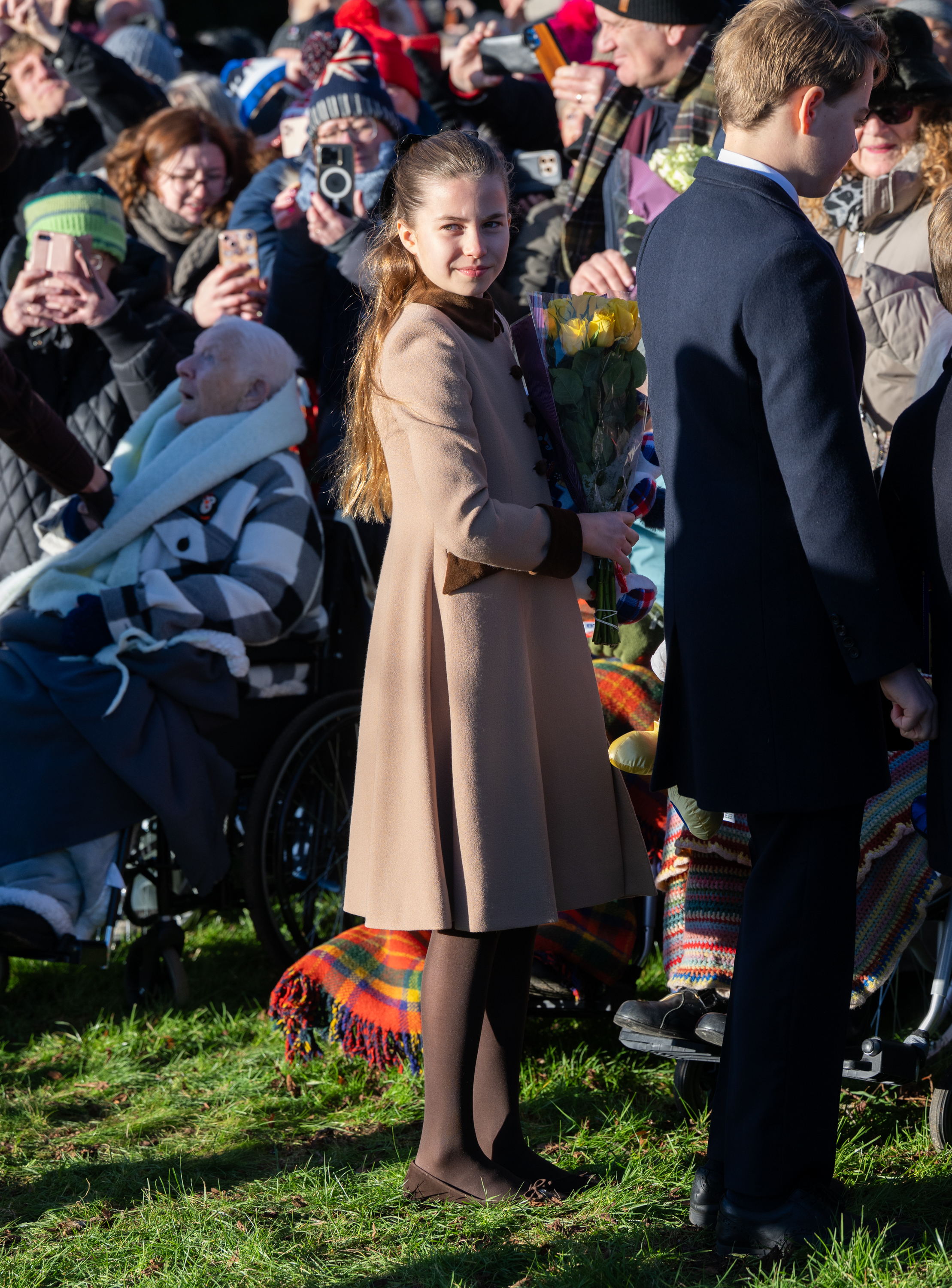 Princess Charlotte wearing a brown coat standing in front of crowds on Christmas day