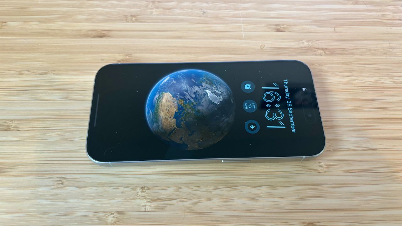 A grey titanium iPhone 15 Pro camera phone on a wooden desk