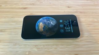A grey titanium iPhone 15 Pro camera phone on a wooden desk
