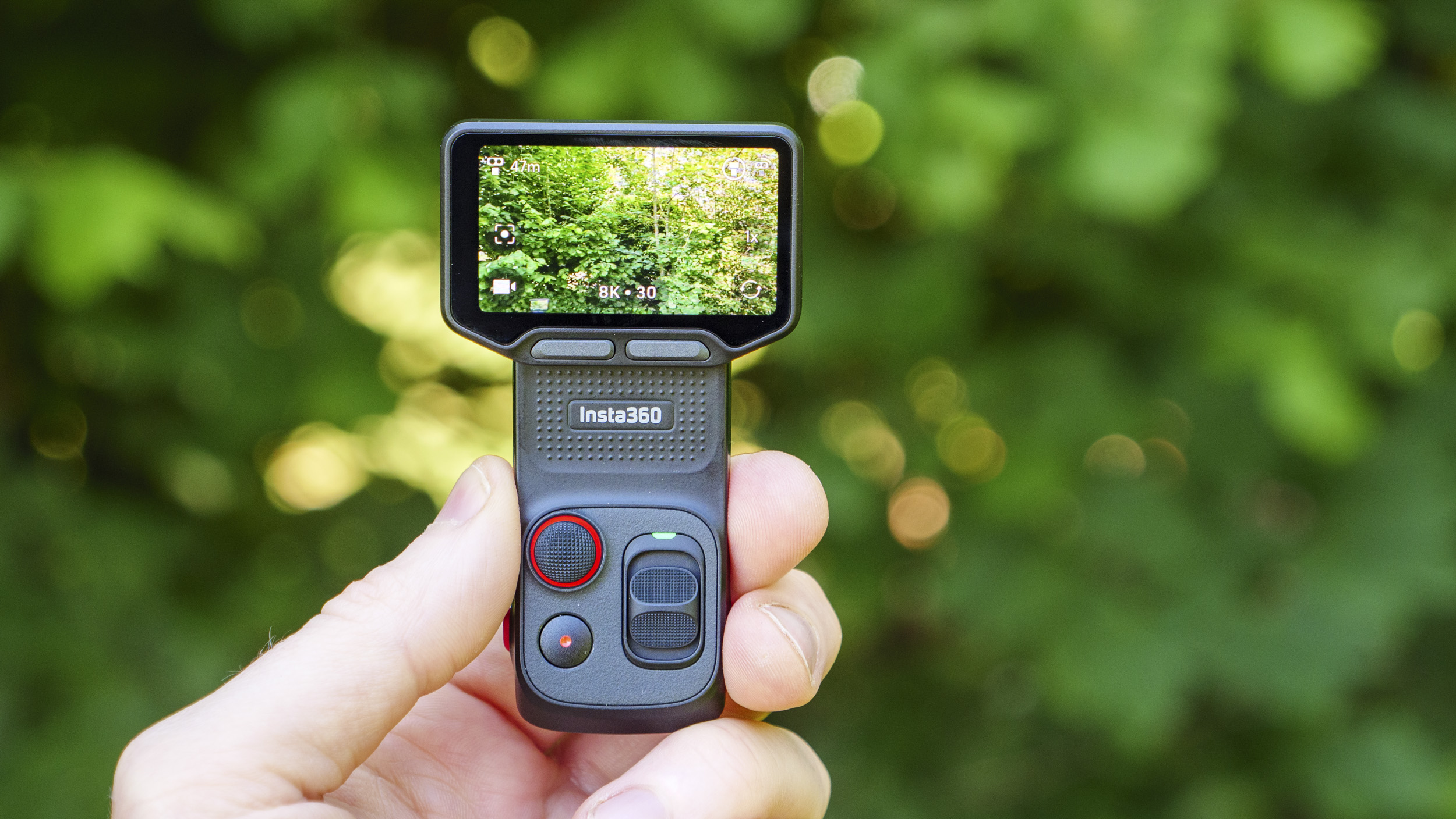 Closeup of the Insta360 Luna Ultra vlogging camera's detachable monitor in person's hand, leafy background, screen in horizontal format