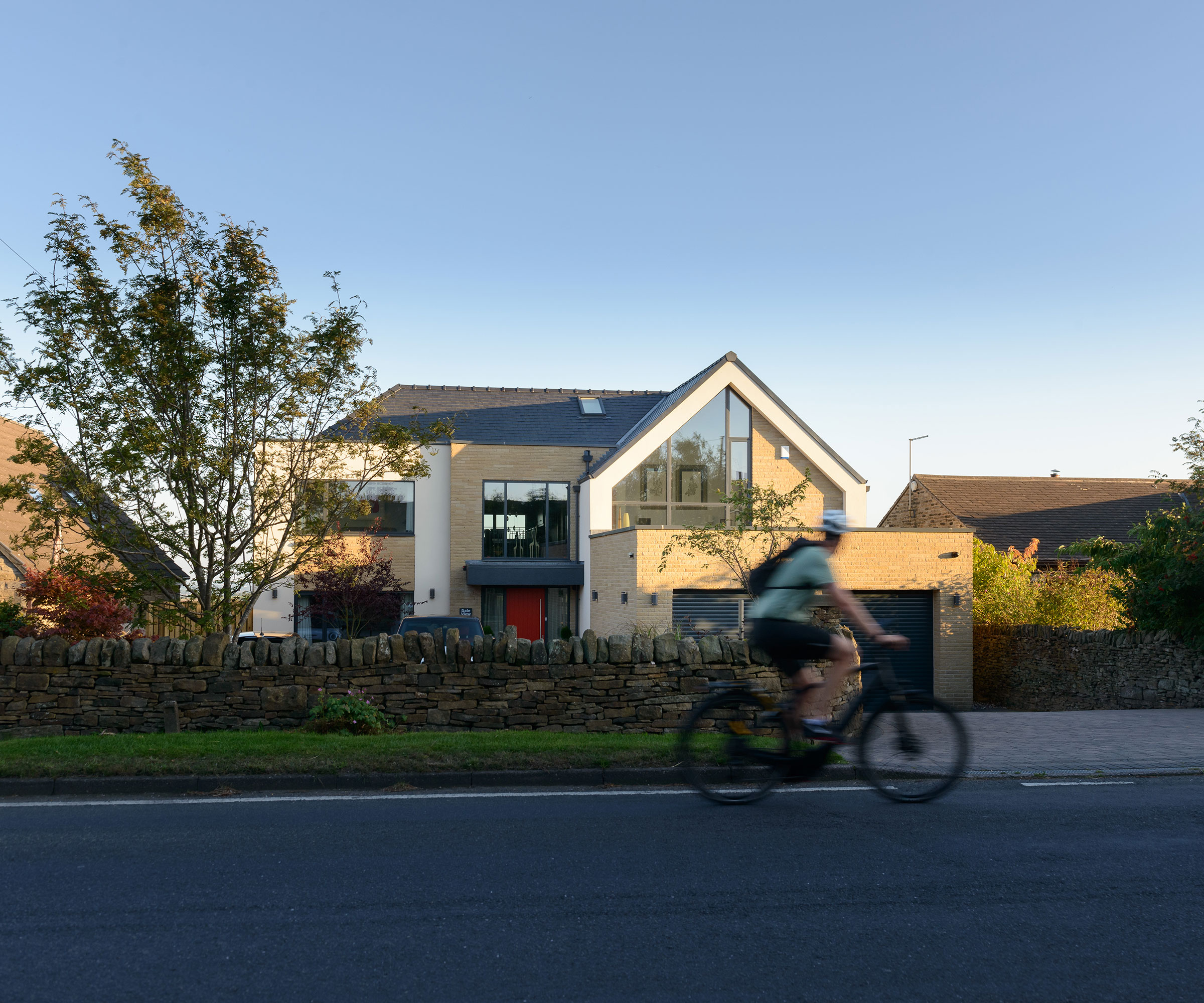 person cycling on a bike in front of a large modern detached house