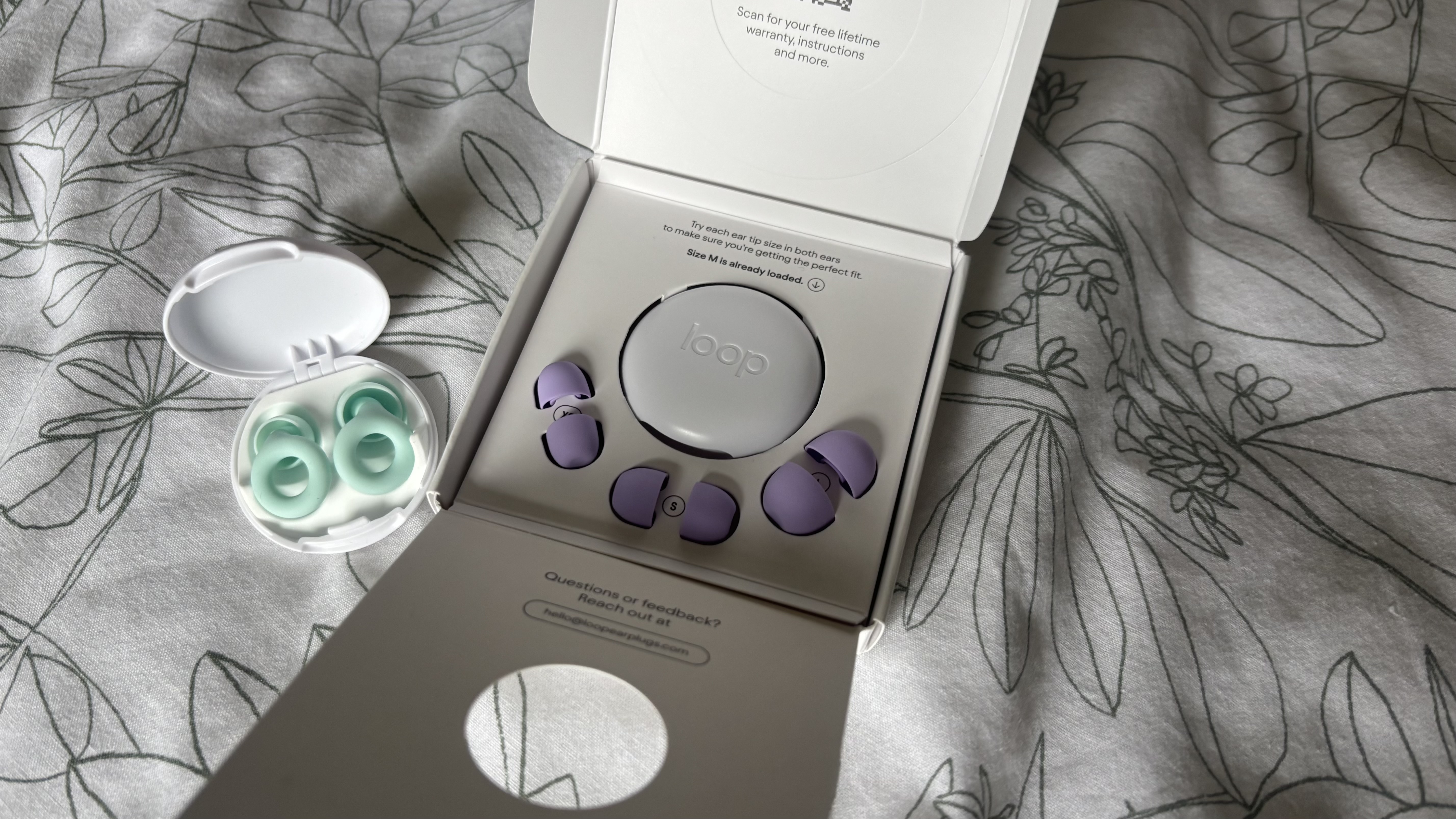 A pair of green Loop Quiet 2 earplugs next to a a boxed pair of violet Loop Quiet 2 earplugs.