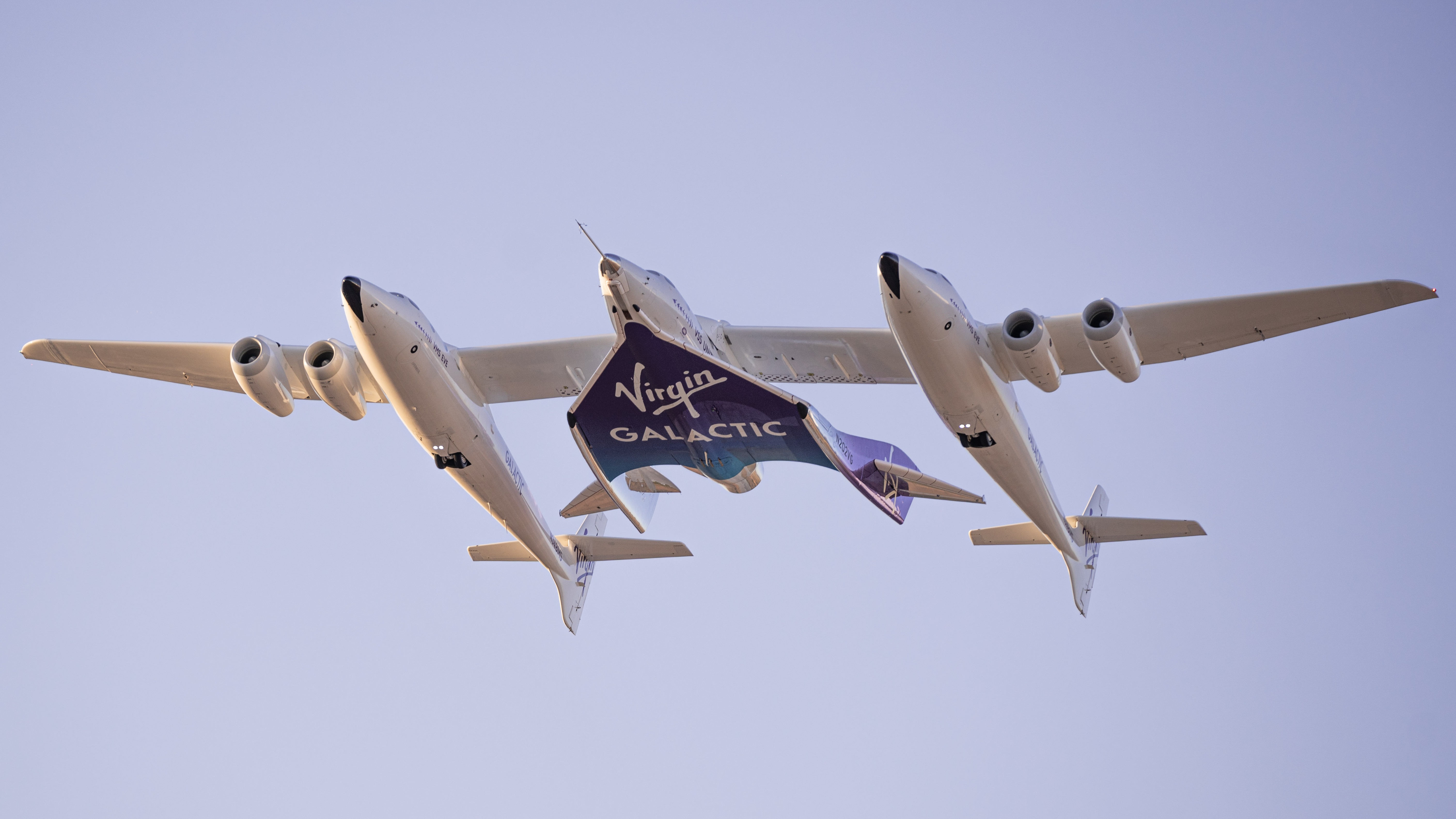 a white space plane is carried in the sky by a twin-fuselage aircraft