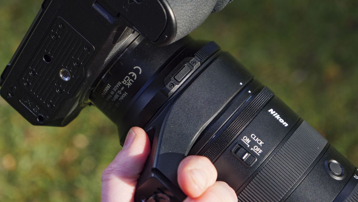 A hand holding Nikon Z 70-200mm f/2.8 VR S II lens by its tripod collar