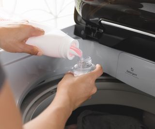 Someone pouring liquid laundry detergent into a cap