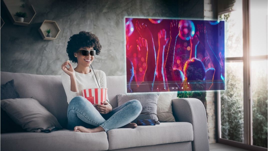 A person wearing the Lenovo Glasses T1 on a couch, using them to watch a show while eating popcorn