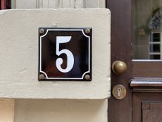 House number 5 on the outside of a residence with a wooden door and brass knob