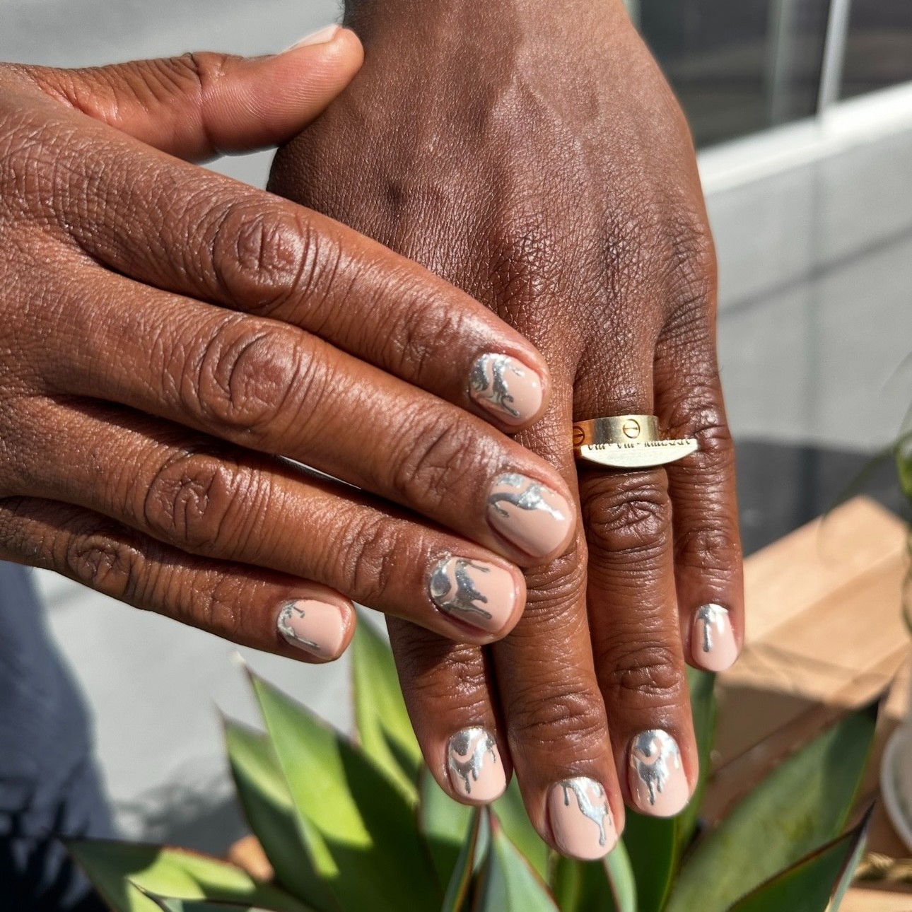 A pair of hands with a nude manicure and silver drip art detailing.