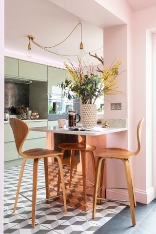 A small pink and green kitchen with breakfast bar peninsula, geometric floor tiling and white countertop