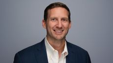 A headshot of Joel Hron, CTO at Thomson Reuters, stood against a grey background.